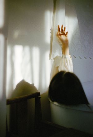 一个小女孩正在窗口向外看 看到一个房间里有白色的窗帘和床。