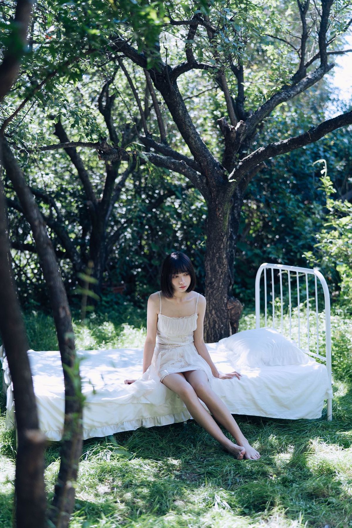 一个年轻女子坐在一片树木和草丛中的白色床上