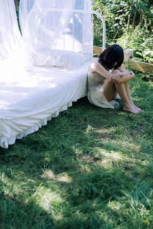 一个年轻女子坐在有顶的白床铺上 花园里