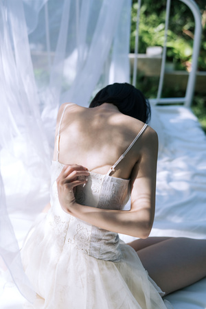 一个穿着白色连衣裙的年轻女子坐在床上