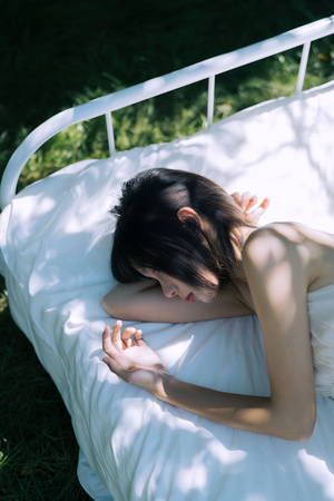一个年轻女子躺在铺有白色床单和白色枕头的床上 双手放在床上 床上有人正在睡觉。
