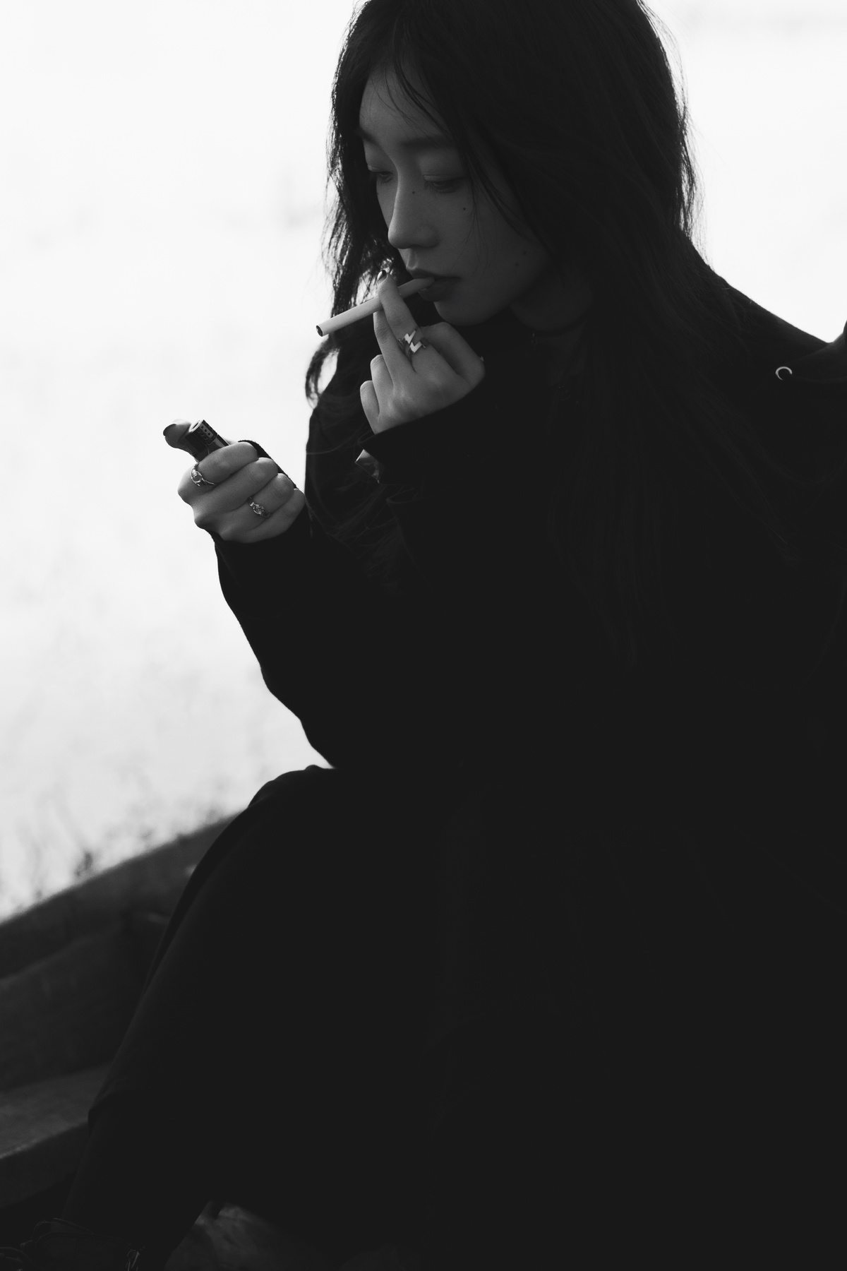 一张黑白照片 一位年轻女子坐在长凳上抽烟。