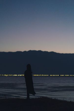 一位女性在海滩上站立 黄昏或日落时分 眺望着一片水域的剪影。
