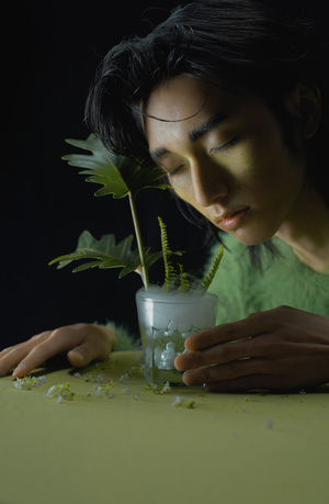 一位年轻女子在一个装满水的绿色花瓶里拿着一株小植物放在桌子上