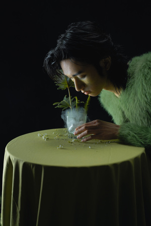 一个年轻女子坐在绿色桌子旁 手里拿着一杯水和一束花。