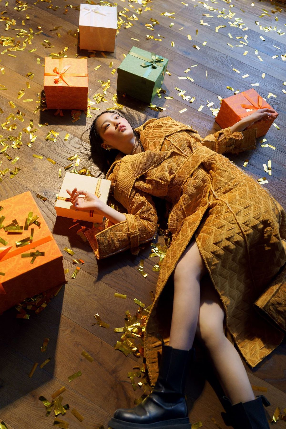 一个穿着连衣裙的年轻女子躺在地上 周围堆满了礼物和彩纸屑。