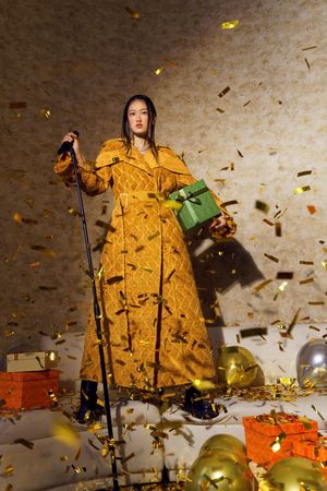 一个穿着黄色连衣裙的女士手持绿色话筒站在舞台上 周围散落着彩纸。