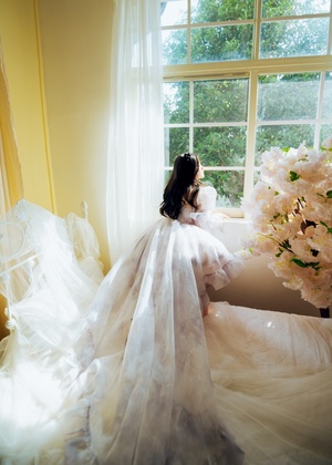 一位穿着白色婚纱站在窗前拿着花束的女人