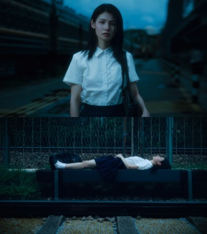 一个穿着白衬衫的年轻女子坐在长凳上 而另一个人躺在铁路轨道上。