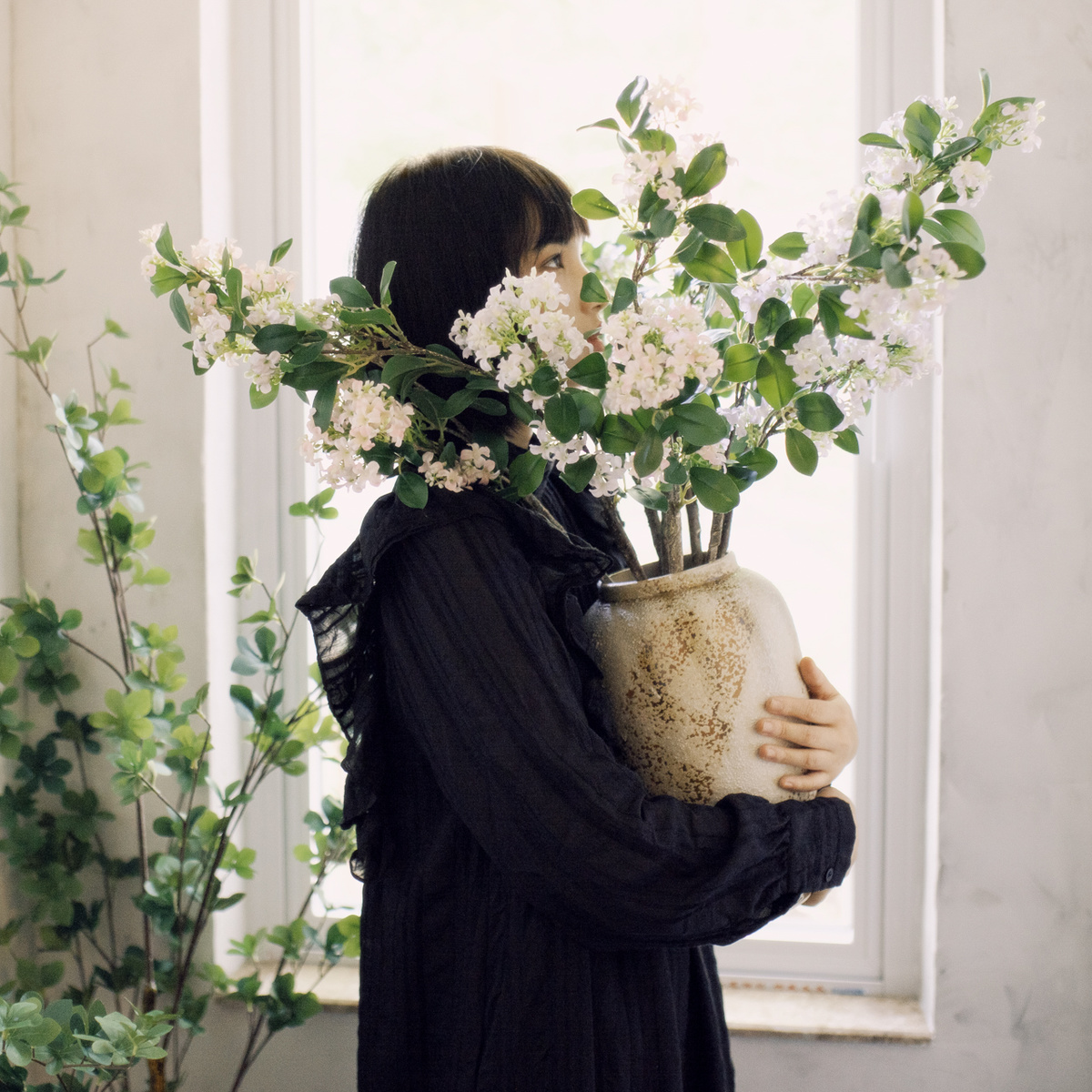 一位年轻女子在一个有窗户的房间里拿着一个插着白色花朵的花瓶