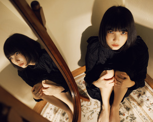 一个年轻女子坐在床上 凝视着镜子里的自己的倒影。
