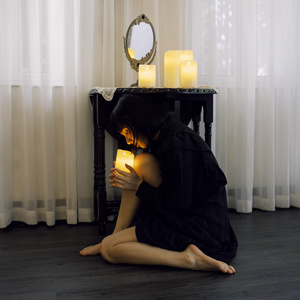 一个年轻女子坐在房间的地板上 手里拿着一支点燃的蜡烛 对着自己的脸。