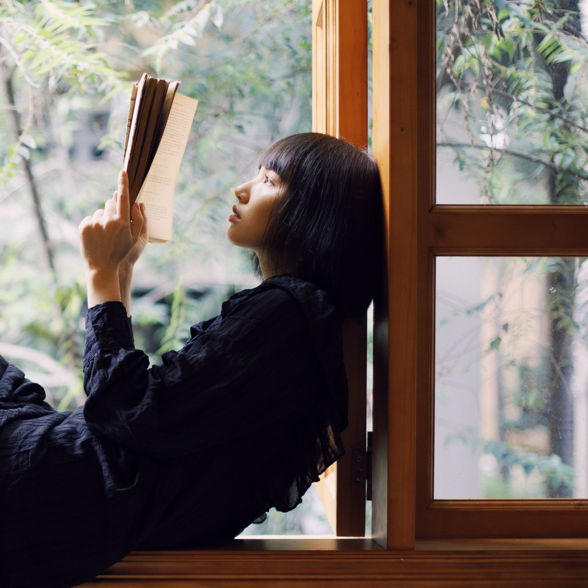 一位年轻女子在窗台上阅读一本书
