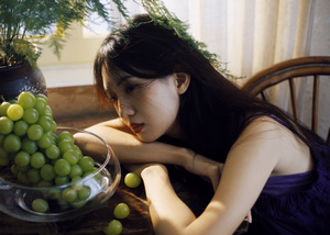 一个年轻女子坐在桌子旁 桌子上放着一盘绿葡萄和一盆植物。