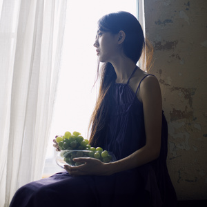 一位年轻女子坐在窗前 手里拿着一碗葡萄。