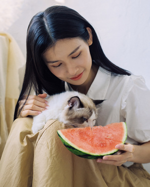 一位年轻女子抱着一只猫和一只西瓜
