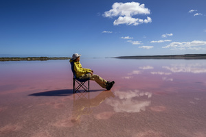 一个坐在椅子上在粉红色湖上放松的人 天空在水中的倒影。
