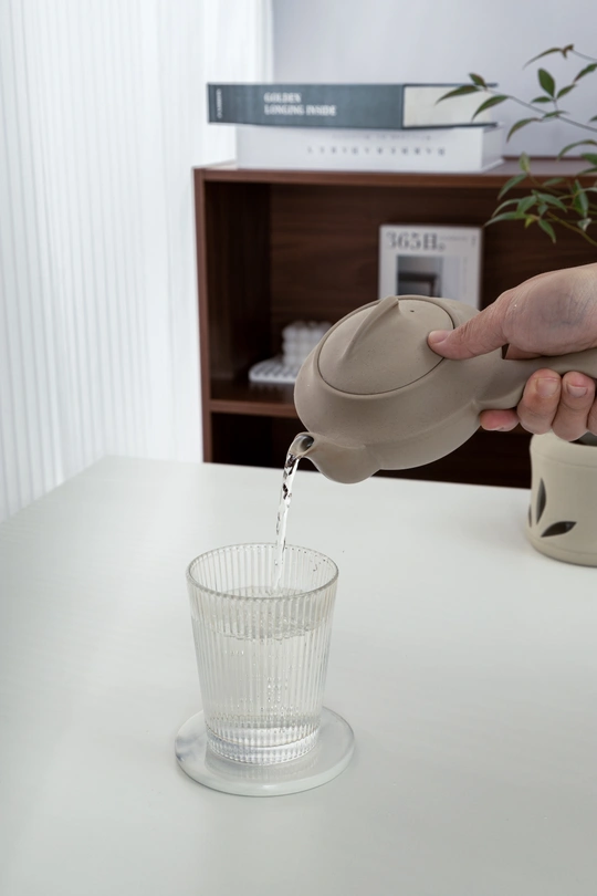 一个人正在从茶壶中倒水到白色的桌子上的一杯水中。