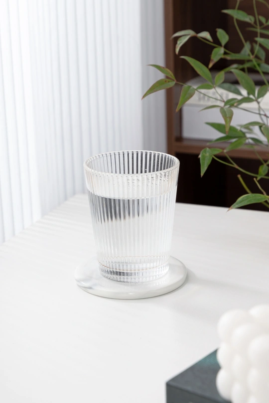 一个放在白色桌子旁边的一盆植物 旁边放着一个清澈的塑料杯。