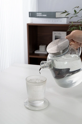 一个人正在从水壶里往桌子上的一杯水里倒水。