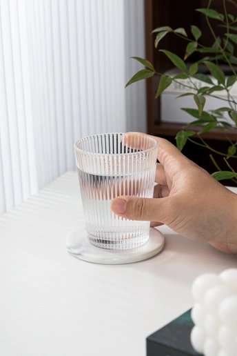 一个人手拿一个透明塑料杯在一张白色桌子上 背景中有植物和气球。