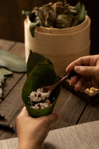一个人手里拿着勺子和筷子 上方是一碗用叶子包裹的食物