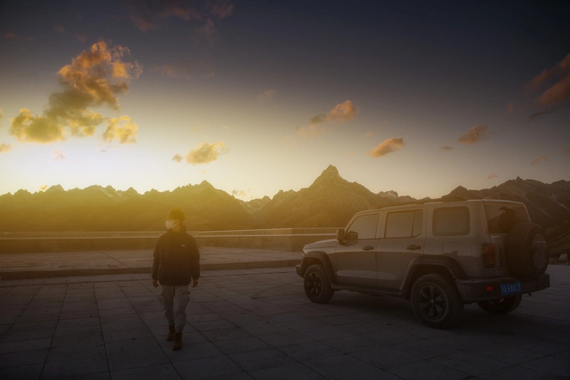 一个男子和一个女子站在停车场 一辆卡车停在汽车前面 夕阳西下 远处是山脉。