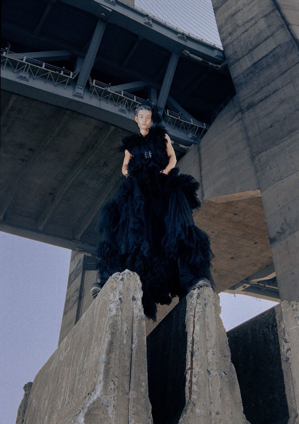 一位穿着黑色连衣裙的女人站在桥下