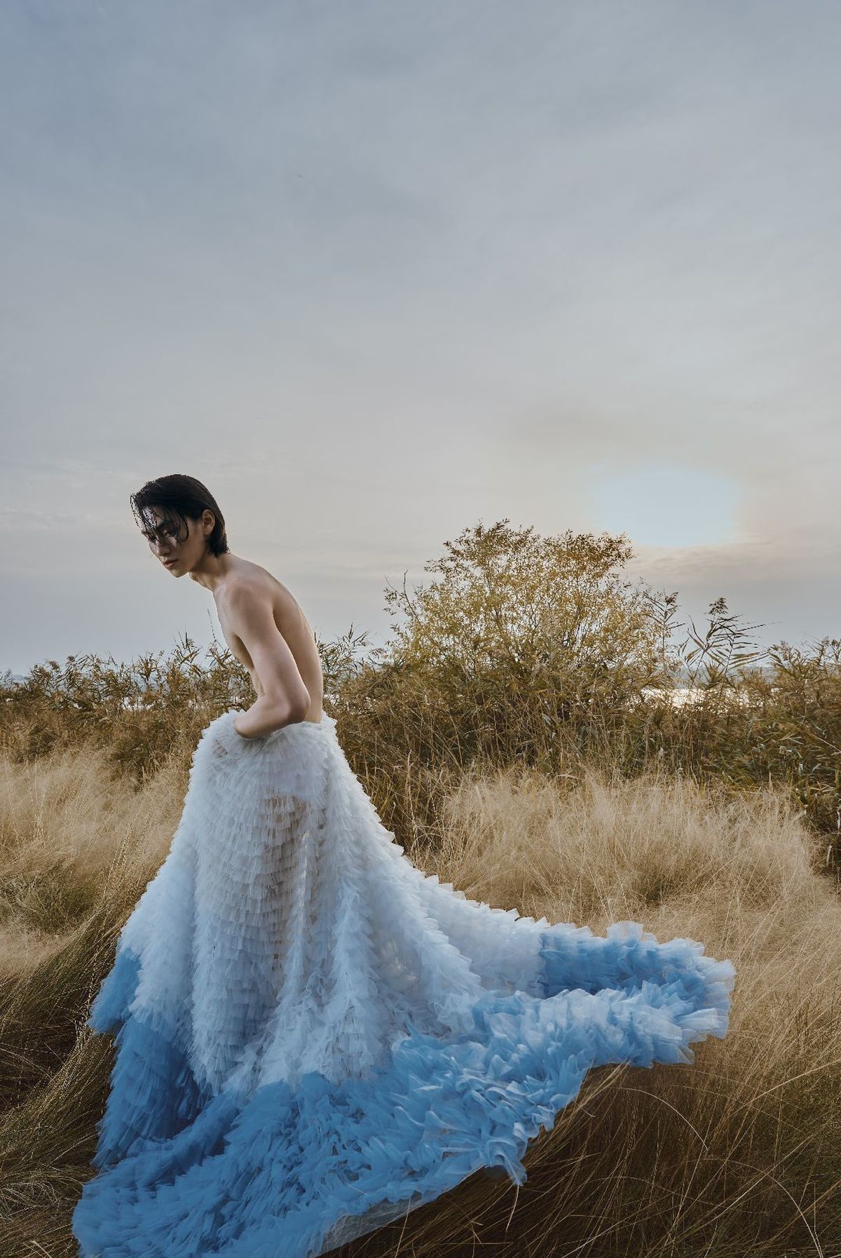 一位穿着蓝色长裙拖尾站在田野里的女人
