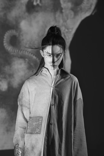 一张黑白照片 一位年轻女子穿着带纹身的夹克站在黑色背景前