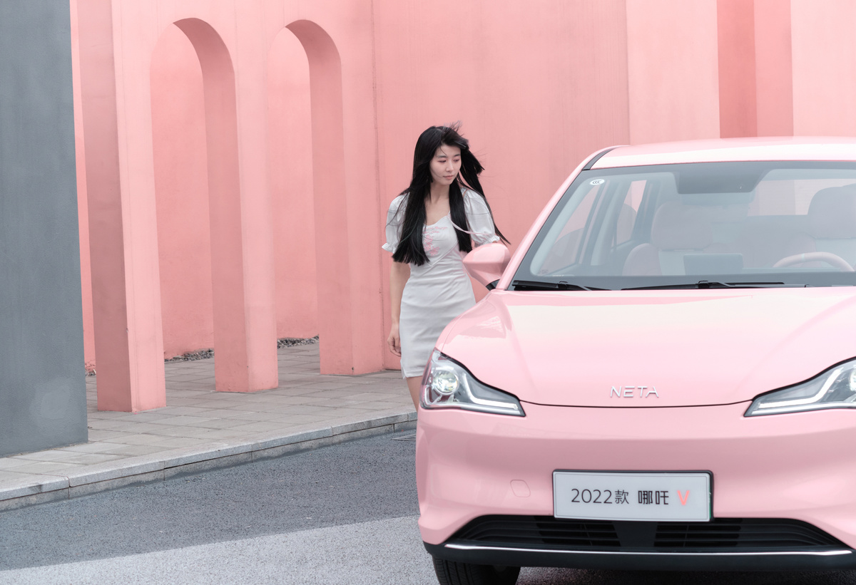 一位穿粉色裙子的女人走在街上 一辆粉色汽车驶过。