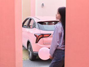 一位拿着气球的女士走在靠近粉红色建筑 带有粉红色门的道路旁边。