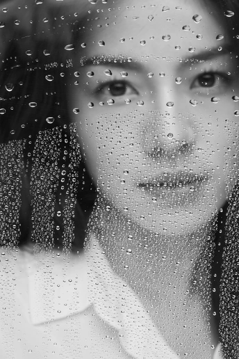 一位穿着衬衫和领带的年轻女子正在通过窗户看水滴 窗户上有水滴。