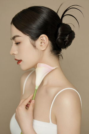 一位年轻女子戴着围在脖子上的发髻 手里拿着一朵粉色花。