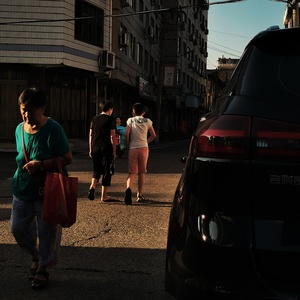 一个背着袋子的女人走在停着的汽车旁边的街道上