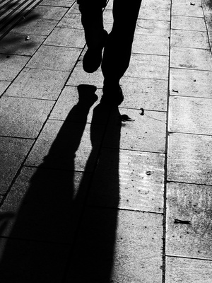 一个人走在长椅旁的人行道上的长长的影子