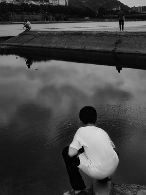 一个小男孩坐在水边的岩石上 一个男人坐在湖边
