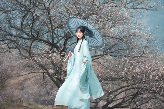 一位穿着蓝色连衣裙 手持雨伞站在盛开树下的女人