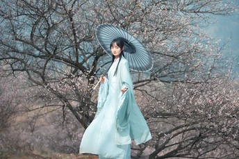 一位穿着蓝色连衣裙 手持雨伞站在盛开树下的女人