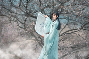 一位穿着蓝色和服的女士 手持白色雨伞 站在雪中。