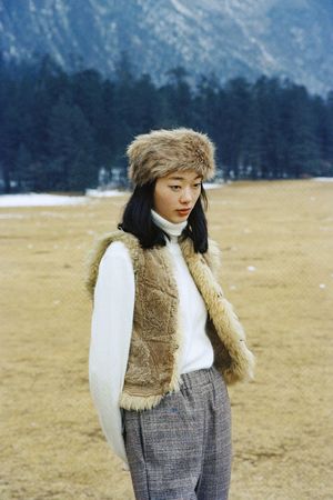 一个穿着皮大衣和帽子站在田野里的年轻女子