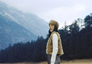 一个穿着皮草大衣和帽子站在田野中 背景是山脉的女孩。