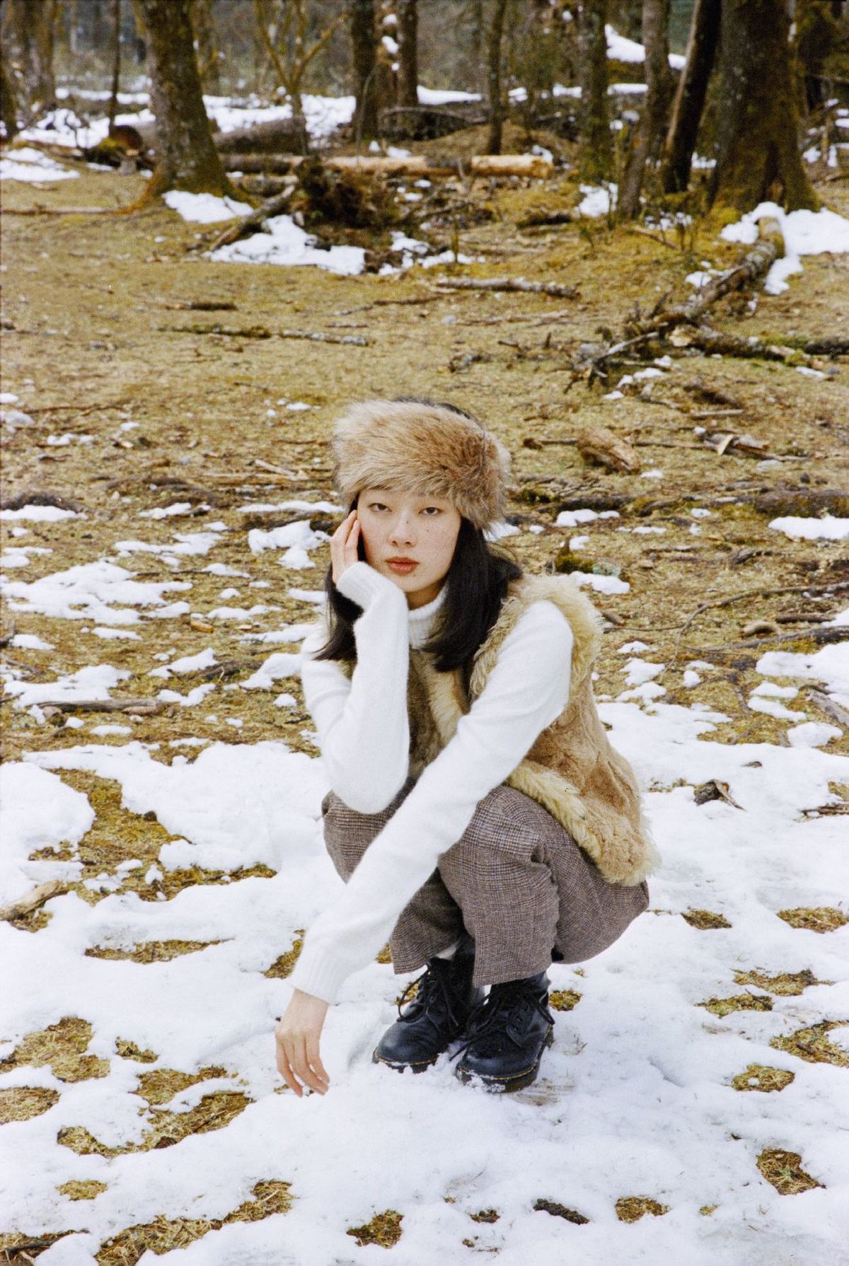 一个戴帽子的年轻女子跪在雪中的森林里
