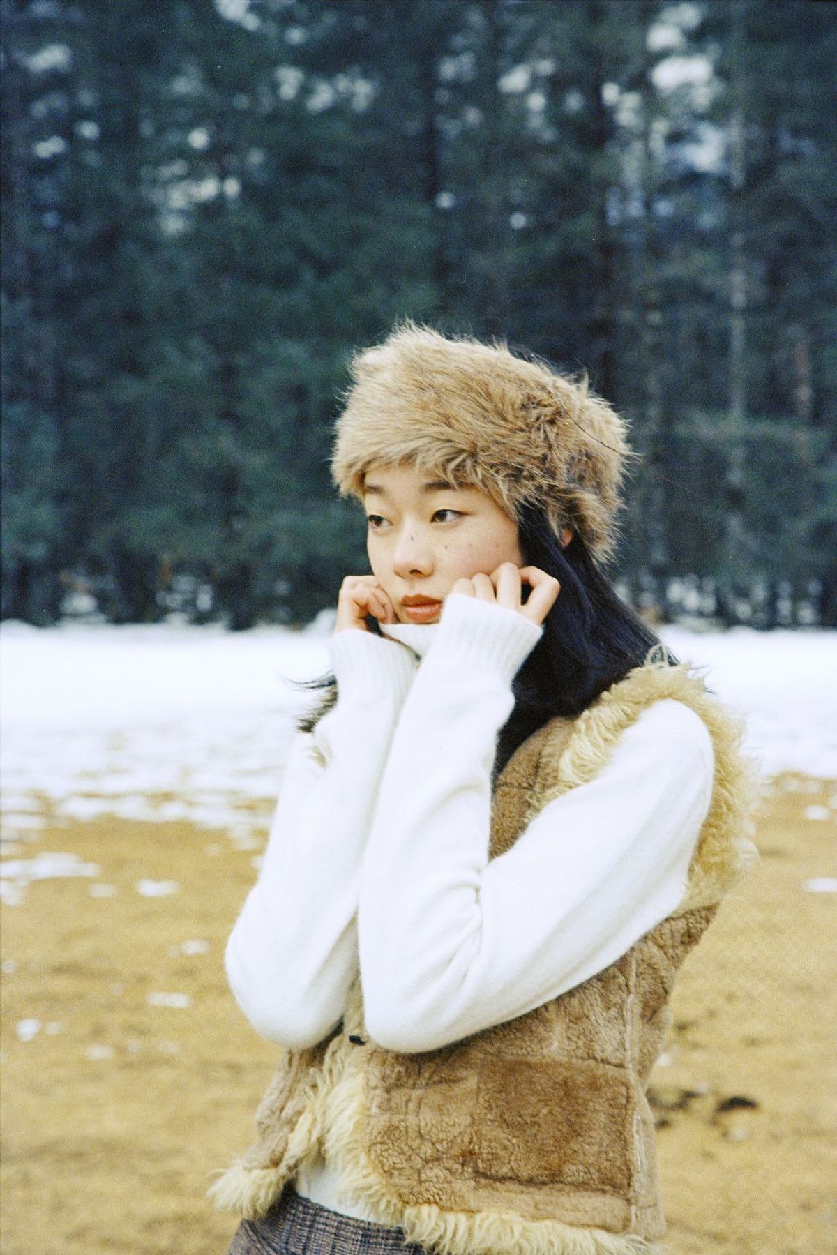 一位穿着白大褂和帽子 正在雪中使用手机交谈的年轻女子。