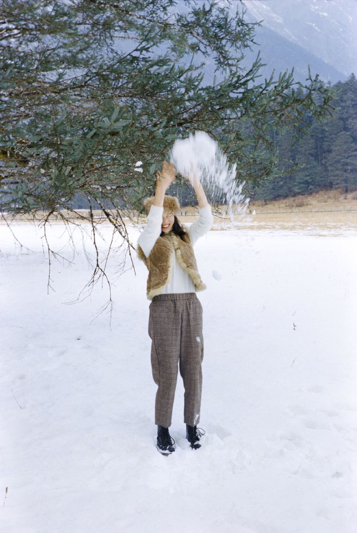 一个站在雪地里的女人向一棵树扔了一个雪球