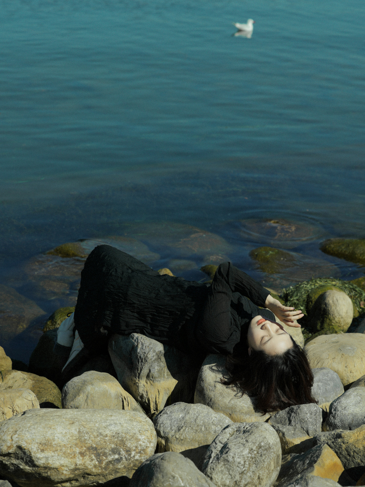 一位年轻女子躺在一些岩石上 靠近水域的岩石岸边。