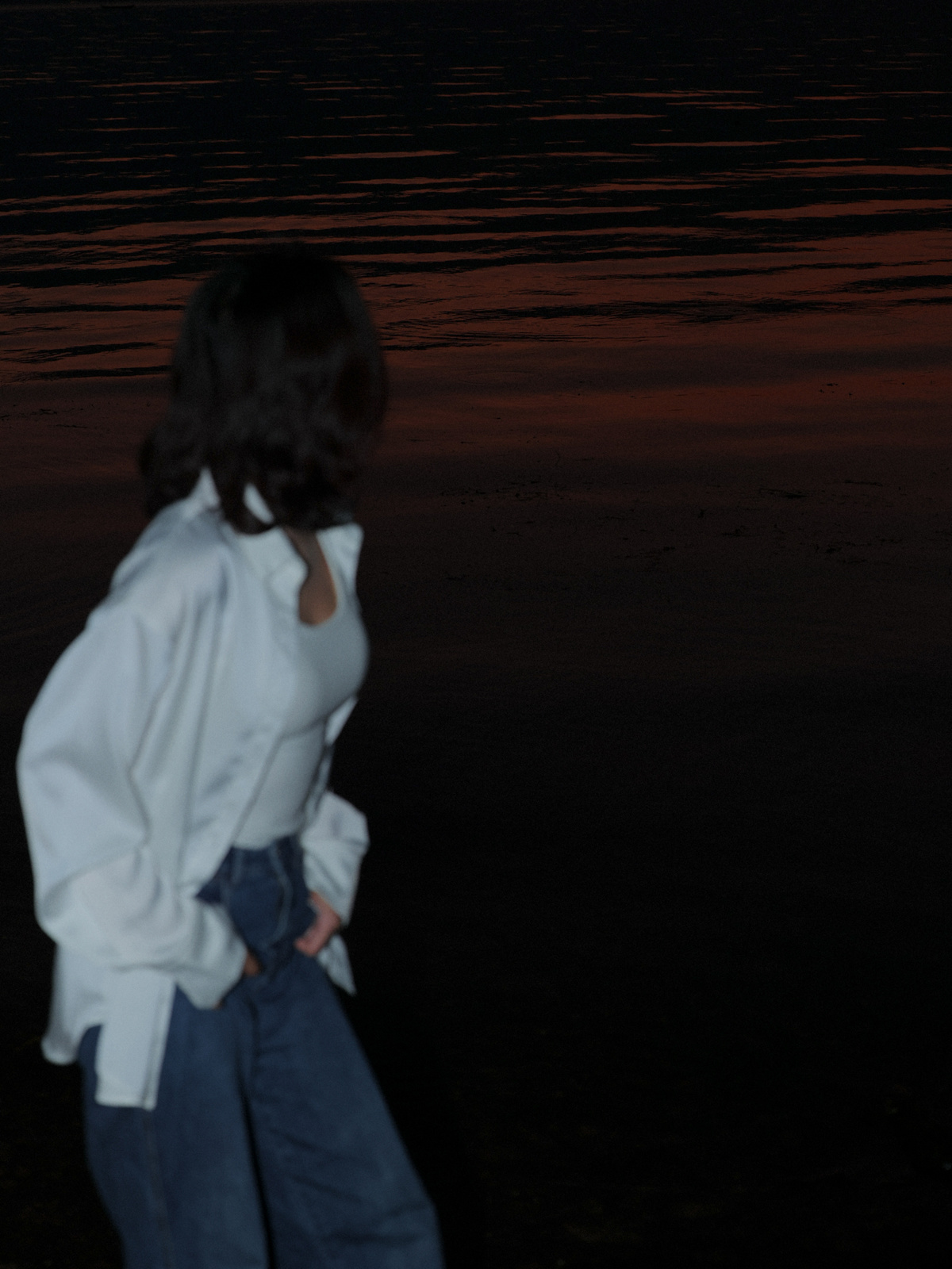 一个穿白色牛仔裤的女人晚上在靠近水的海滩上散步