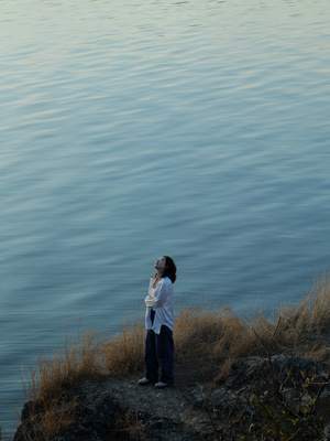 一位妇女站在岩石上 从岸边向外眺望水域。