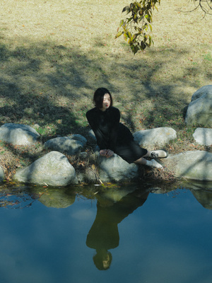 一个人坐在水边的一块石头上 一个女孩也坐在那块石头上。