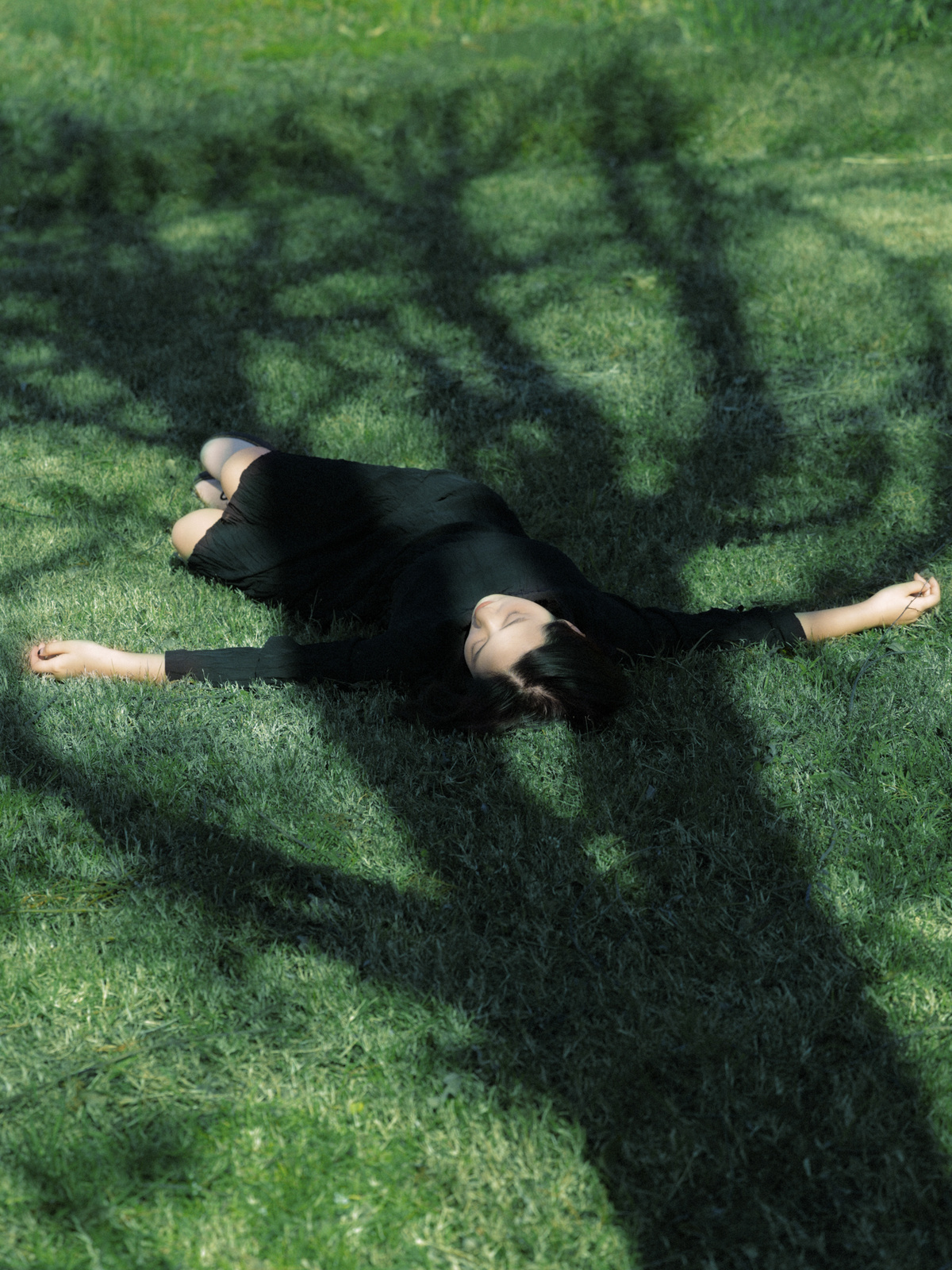 一个女人在绿色的草地上 在树荫下躺着 草地上有一个飞盘。